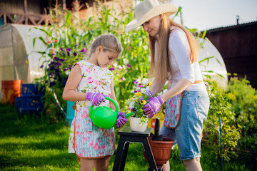 Woman gardener helping her daughter to pour garden flower pot.
