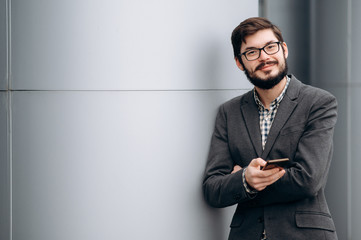 Stylish portrait of young guy in a suit with a beard, glasses and a phone in his hand, with a...