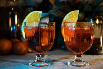 Two homemade alcohol cocktails. Red liquid with orange in wine glasses on the table.