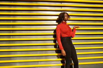 Portrait of a curly haired african woman wearing fashionable red turtleneck posing against yellow...