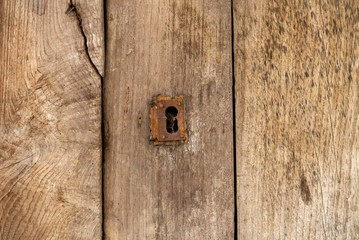 Keyhole and old metal escutcheon on a distressed grungy wooden door, close up texture view