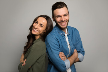 Kind and cheerful. Two lovers in casual clothes are standing back to back with cheerful facial expressions, posing with folded arms and looking in the camera.