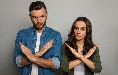 Stop doing this. Close-up photo of a serious couple in casual outfits, who are looking in the camera with their hands crossed as a sign of refusal.