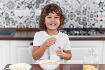 Happy boy feels happiness while eating healthy breakfast of cornflakes and milk at the kitchen.