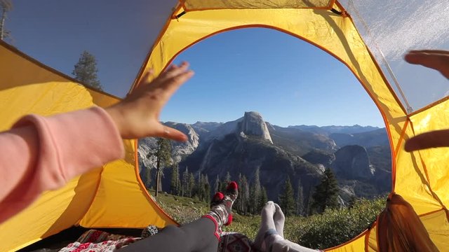 A couple has a day out in Yosemite Valley, admiring the beauty of Sierra Nevada mountains and the Half Dome rock from the tourist tent. They make a hand heart against the backdrop of the landscape.