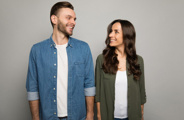 My other half. A handsome man and a beautiful woman in casual clothes are gently looking into each other’s eyes, standing in front of the camera and smiling.