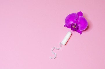 tampon as a remedy for critical menstrual days with flower orchid on pink background. hygiene, care and cleanliness of woman. copy space for text