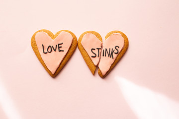 Two broken heart gingerbread cookies decorated with pink fondant with the message love stinks. heartbreak concept.