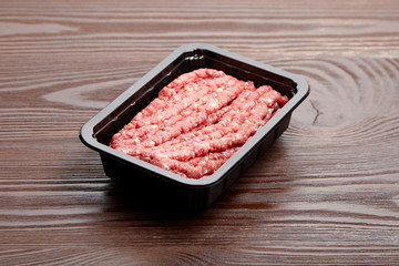 Ground beef in a black plastic tray on wooden table. Uncooked mincemeat. Forcemeat, fresh raw minced meat