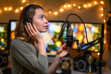 A girl radio host in a cozy atmosphere broadcasts with a studio microphone. Stream, live broadcast,...