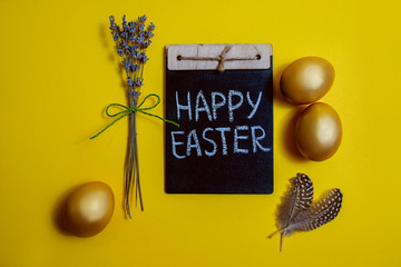 Happy Easter inscription on chalk board, golden chicken eggs on a yellow background