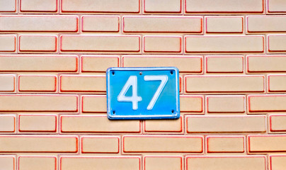 Fototapeta na wymiar Number 47, forty-seven, a blue plate on light brown brickwork background.