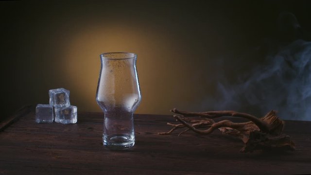 empty beer pint on a wooden table with ice, smoke rises against the background