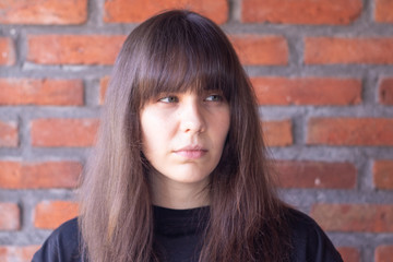 Portrait of a sad brunette woman with bangs wearing a black t-shirt on brick wall background