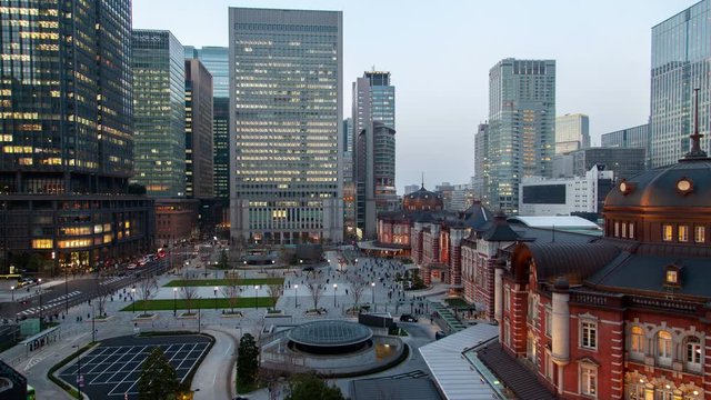 Timelapse Tokyo old railway station square with people flow among office skyscrapers from twilight to illuminated night