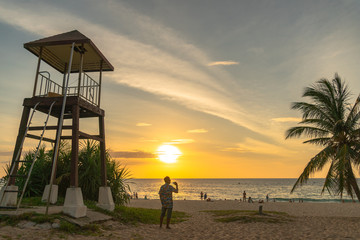 a man walking and take photo around lifegaurd tower during sunset at Karon beach Phuket