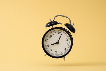 Small black alarm clock in front of yellow background