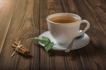 A Cup of tea with cinnamon and green leaves on a wooden table.