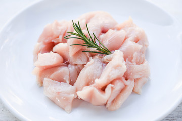 Pieces of raw chicken meat with rosemary - fresh raw cut chicken fillet on white plate background