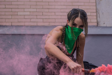Beautiful young feminist activist dressed in black with face covered with a green bandana and...