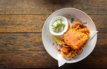 Fish and chips with tartar sauce in a plate on a wooden table background.