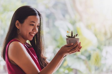 Asian smiling woman holding and looking at the cactus in the planted pot.Concept idea of planting...