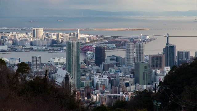 Timelapse Kobe downtown district with skyscrapers and industrial area across bay view from hill top with tourist cableway