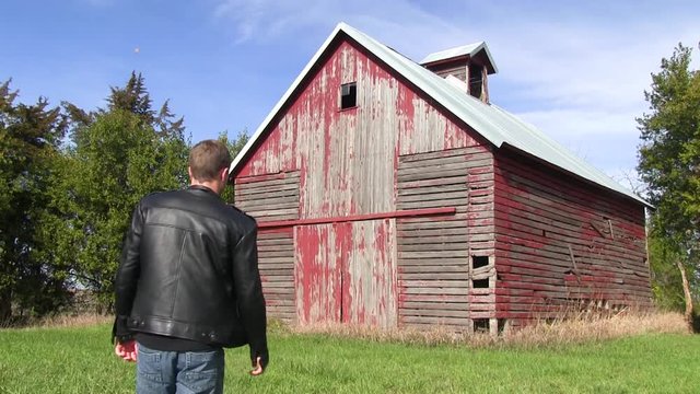 Man in black leather jacket walks toward and old red barn.  The farm is located outside of Ames, Iowa.