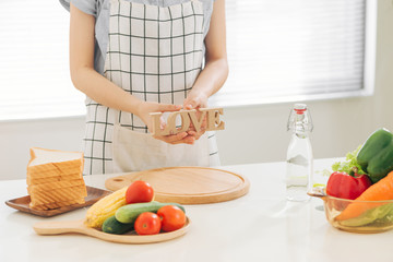 Asian woman with wooden letter LOVE at table with toast and vegetables in kitchen at home