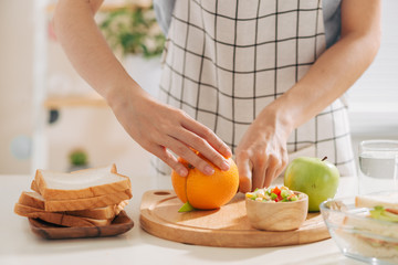 Close-up of lady arms cutting orange by knife into slices.