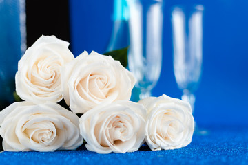 Two glasses of cold champagne and a bouquet of white roses on classic blue  background. Saint Valentine's and women's day  concept.