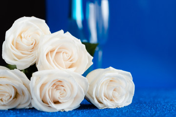 Fototapeta premium Two glasses of cold champagne and a bouquet of white roses on classic blue background. Saint Valentine's and women's day concept.