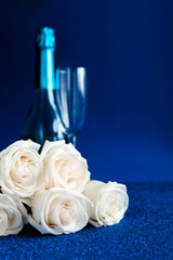 Two glasses of cold champagne and a bouquet of white roses on classic blue  background. Saint Valentine's and women's day  concept.