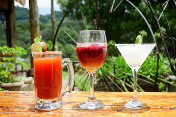 Glasses and jar with drinks prepared with alcohol placed on outdoor table on sunny day, social celebration in Guatemala.