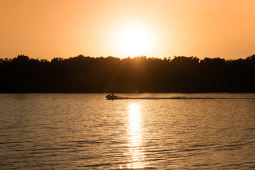A male cruising along the river on a fast wave runner, high contrast scene of picturesque sunset.