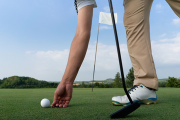 Golfer using pin marking position of golf ball  on green.