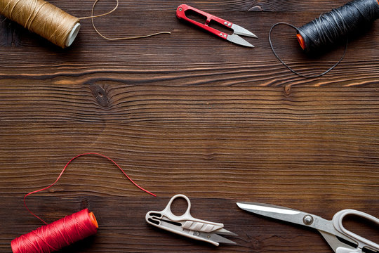 Tailor's work desk. Thread and sciccors on dark wooden background top-down copy space
