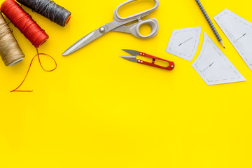 Clothes designer work desk. Pattern, scissors, thread on yellow background top-down copy space