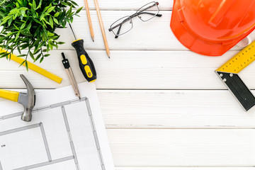 Builder work desk with hard hat, instruments and blueprints on white wooden background top-down frame copy space