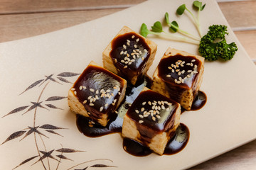 Tofu no Dengaku is grilled Tofu with sesame seed and Hatcho Miso Sauce on brown plate and wooden background.