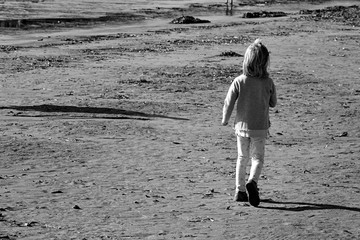 Small girl walking alone down the sand beach