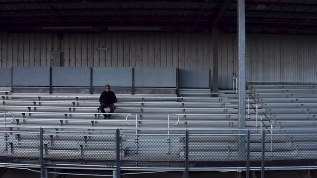 Tracking shot of retired coach sitting in empty bleachers