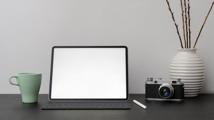 Close up view of blank screen tablet  with coffee cup, stylus and camera on black desk with white wall