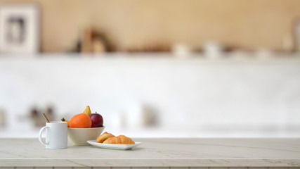 Close up view of fruit bowl, coffee cup and croissant on marble desk with blurred kitchen room