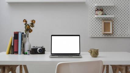 Close up view of office room with blank screen laptop, office supplies, camera, coffee cup and decorations on withe wooden