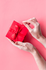 Unpack a gift on Valentine's Day. Women hand hold ribbon tied present box on pink background top-down