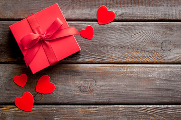Gift to a sweetheart on Valentine's Day. Red present box near hearts on dark wooden background top-down copy space