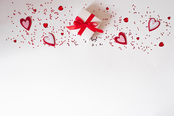 Border of gift with red bow, glass and felt hearts on white background with confetti