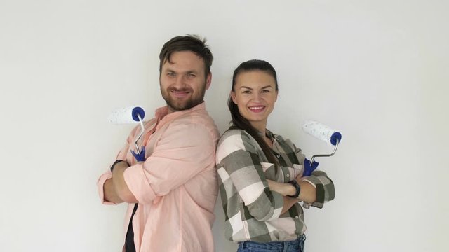 Happy young couple with paint rollers near white wall