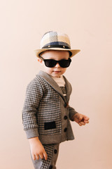 Happy baby boy in grey suit, hat and glasses on light background